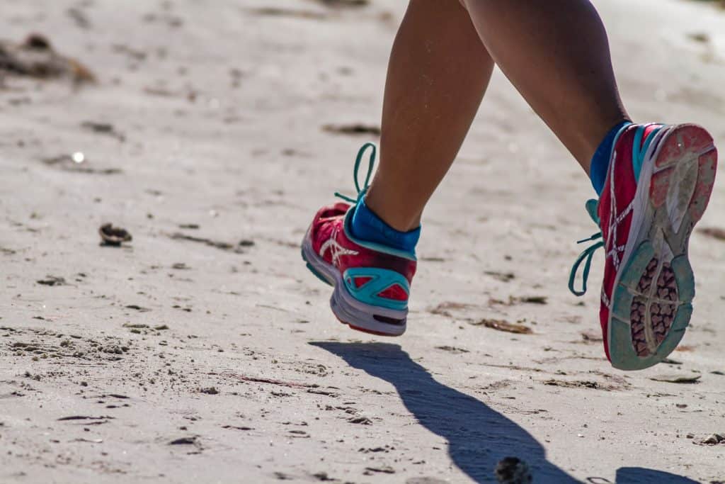 A person wearing aqua shoes running on a beach.
